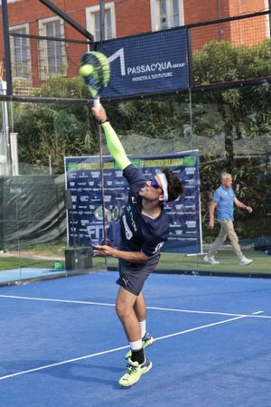 Player serves during padel tennis match on outdoor blue court.
