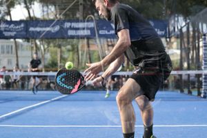 Player hits backhand shot during padel tennis match on blue court.