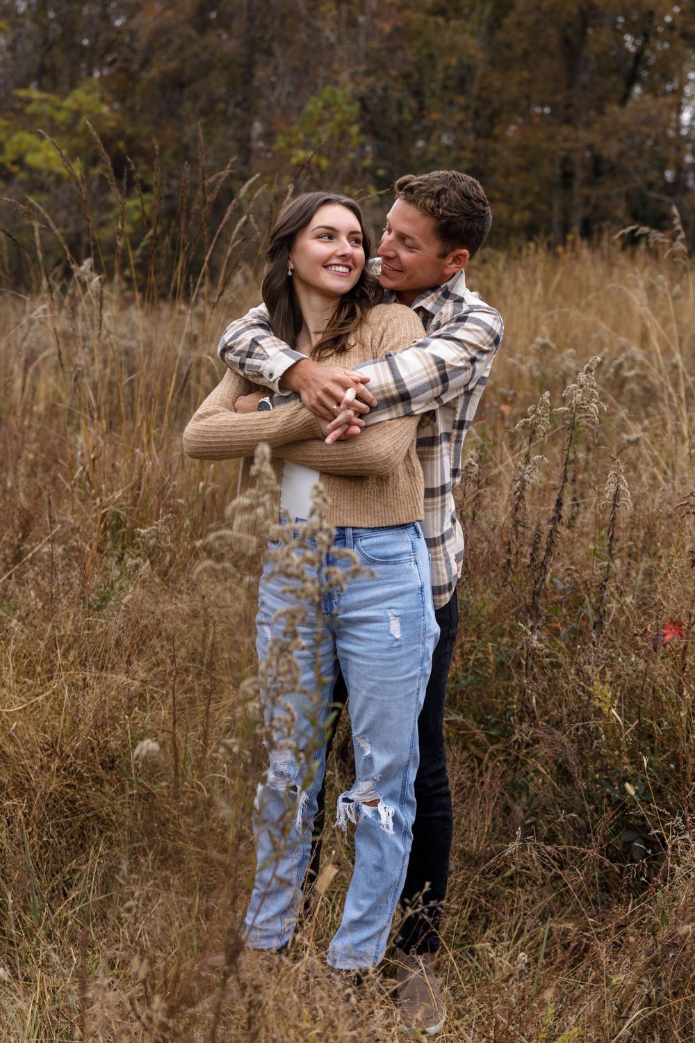A romantic embrace between a couple in casual fall outfits standing among tall grass.