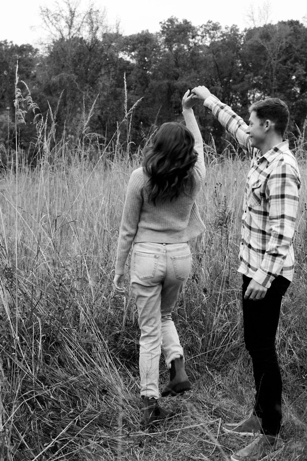 A dancing couple in casual attire twirls in a black and white photo amidst tall grass.