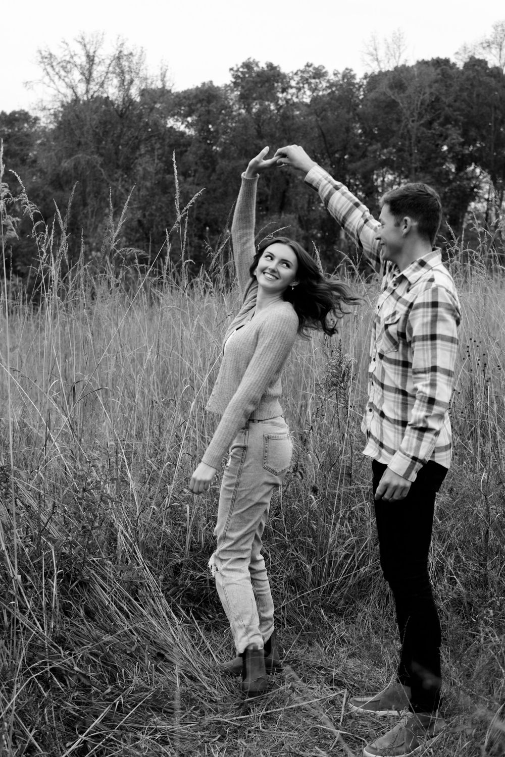 A couple dances in a field captured in black and white as they share a romantic moment.