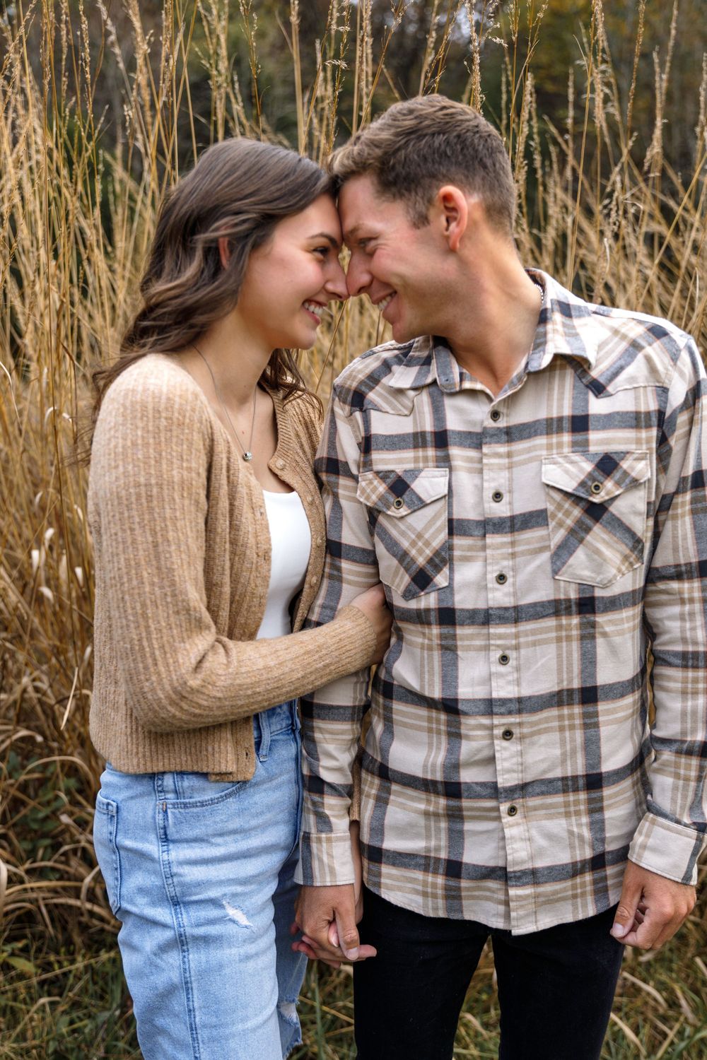 A couple shares an intimate moment touching foreheads in a field of autumn grass.