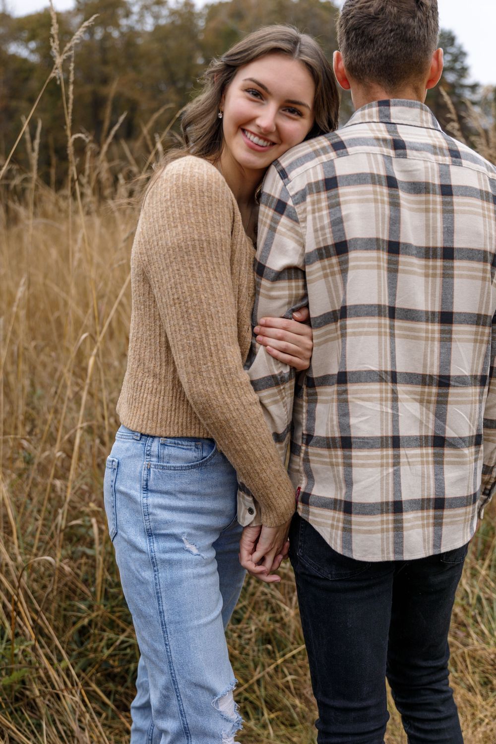 A playful moment captured between a couple in casual attire among autumn grass.