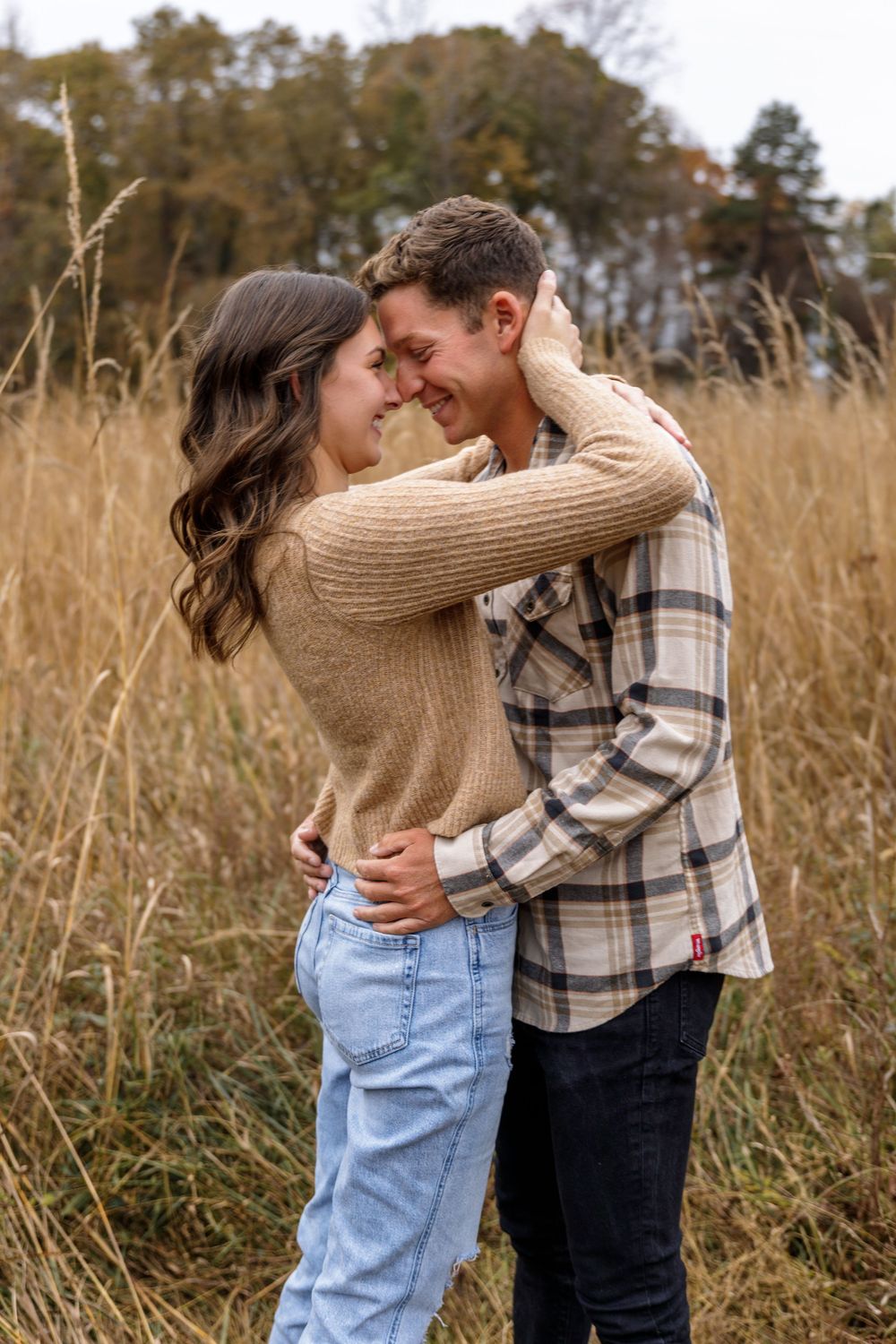 A tender embrace between a couple in casual fall clothing standing in tall grass.