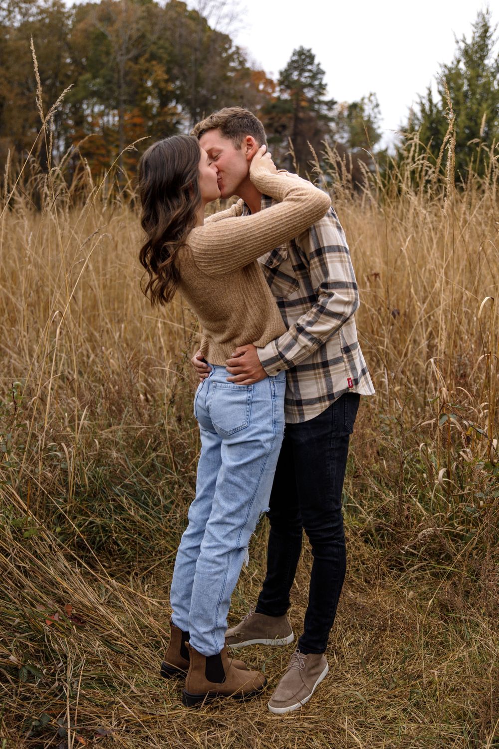 Romantic couple embraces in tall autumn grass during outdoor photoshoot.