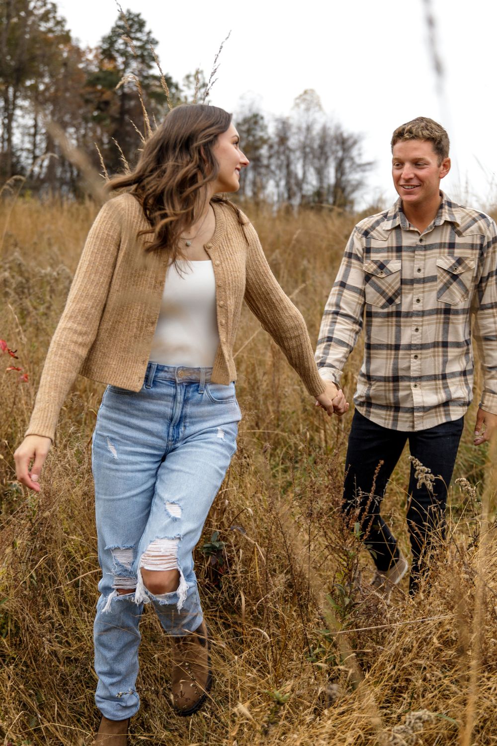 Couple in plaid and denim share playful moment in rustic field setting.