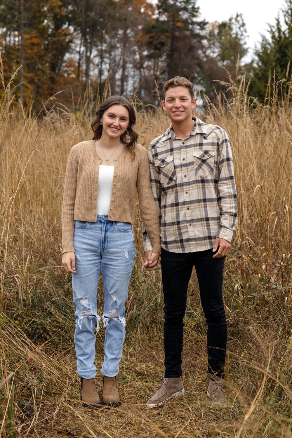 Couple in coordinated fall outfits standing together in tall grass field.