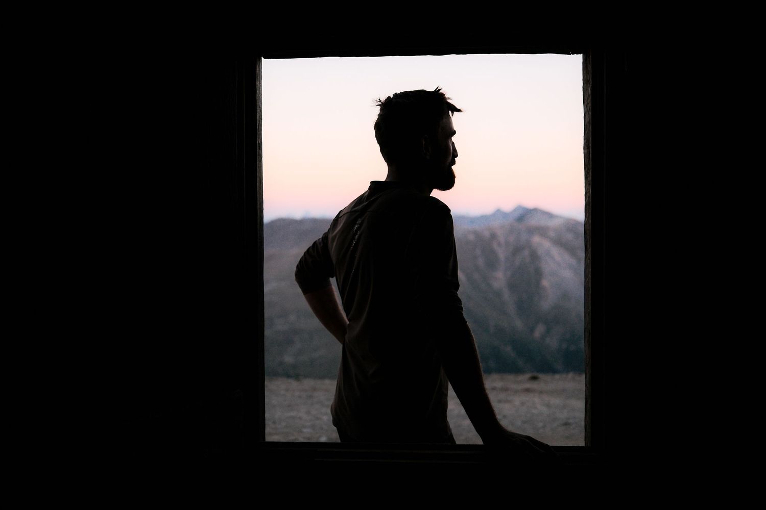 Silhouetted figure stands against a mountain landscape during sunset, creating a dramatic outdoor scene.