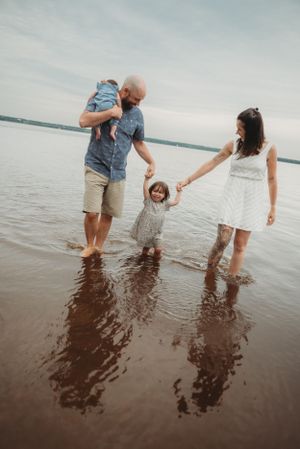 Family standing in shallow water at sunset creating reflections on the calm lake surface.