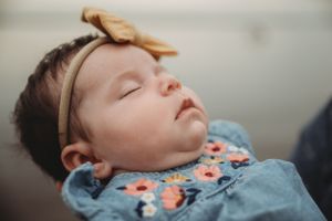 Close-up of a sleeping baby wearing a yellow headband and floral outfit.