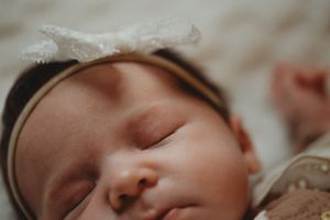 A peaceful closeup of a sleeping newborn baby wearing a delicate headband.
