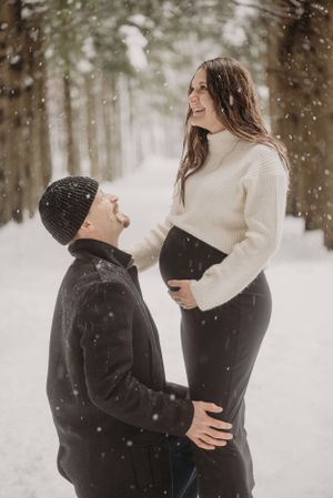 Loving winter maternity photoshoot with couple sharing tender moment in snowy forest.