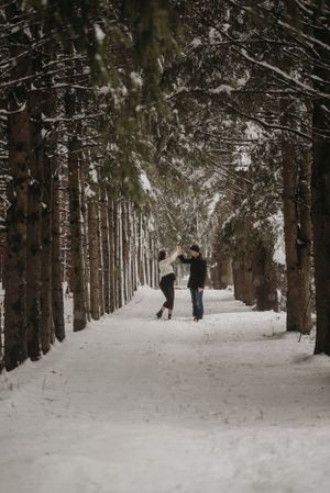 Couple walking down a scenic tree-lined snowy path in winter.