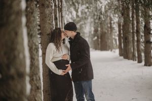 Intimate winter maternity photo of couple by snow-covered trees.