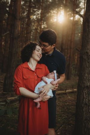 Happy couple in wooded setting holding their baby at sunset.