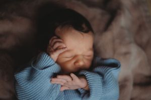 Newborn baby in blue stretches and yawns during an intimate photo session.
