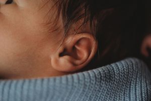 Detail shot of a baby's ear and dark hair against a blue knitted sweater.