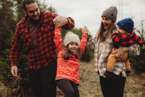 Family holding hands and walking together through Christmas tree farm wearing festive winter attire.