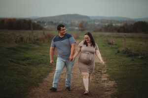Expecting couple walking hand in hand on dirt path during sunset maternity shoot.