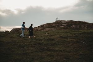 Two silhouettes walking dog along hilltop path during golden hour.