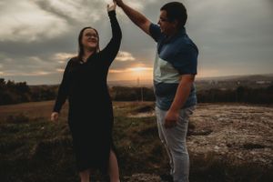 Couple celebrating with raised hands against sunset skyline on hilltop.