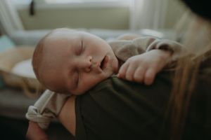 Peaceful sleeping baby resting on shoulder in natural light.