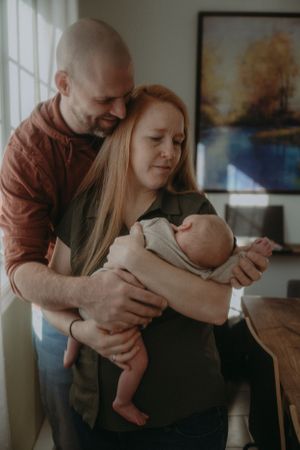 Family shares tender moment with newborn baby near window with art in background.