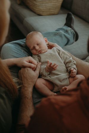 Sleeping infant in gray onesie resting peacefully on a couch while being gently held.