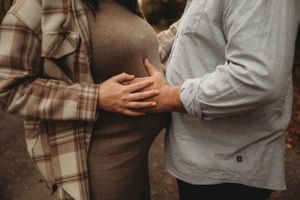 A close-up shot of expecting parents holding hands over a pregnant belly during an outdoor maternity photoshoot.
