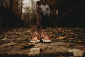 Brown leather baby shoes on fallen autumn leaves with blurred background.