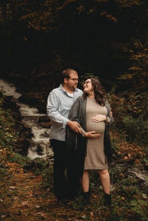 Maternity couple embracing by waterfall surrounded by fall foliage.