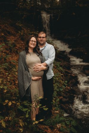 A maternity portrait of an expecting couple embracing by a cascading waterfall in autumn.