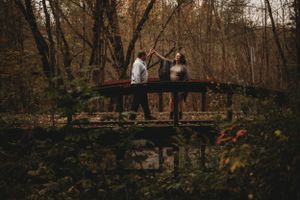 Expecting couple standing on wooden bridge in autumn forest setting.