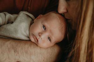 Peaceful infant with alert eyes rests against soft fabric in warm lighting.