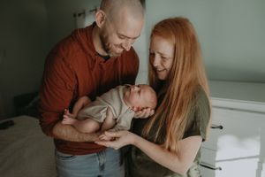 Tender family moment showing gentle interaction with sleeping newborn.