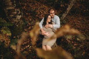 Intimate maternity moment captured through golden fall leaves in forest.