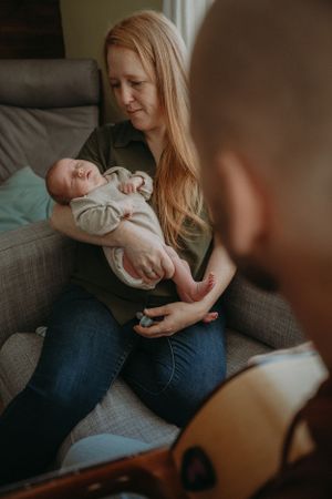 Mother holding sleeping infant on cozy gray couch in natural lighting.
