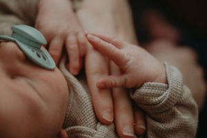 Close-up of tiny baby hand grasping adult finger in emotional moment.