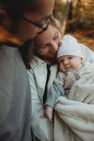 An intimate family moment captured in warm autumn lighting with a baby in white.