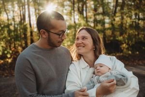 A loving family shares warm smiles in an autumn forest setting during golden hour.
