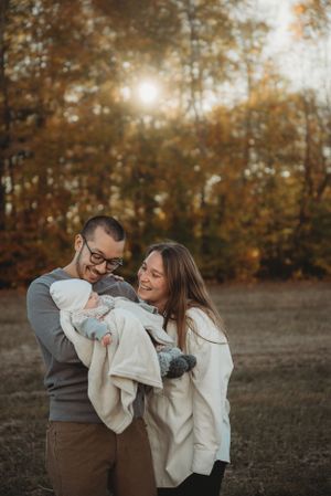 A joyful family shares laughter while holding their baby in a sunlit autumn field.
