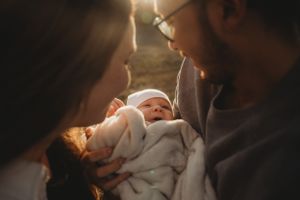 Intimate family moment with newborn baby swaddled in white blanket in warm dramatic lighting.