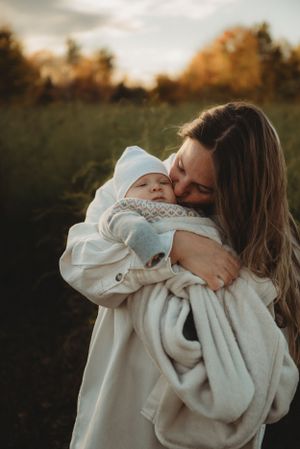 Parent embracing swaddled newborn baby outdoors during golden hour.