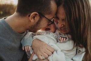 Intimate family moment with newborn baby cuddled between parents outdoors.