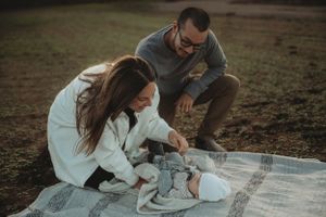 Family having outdoor photoshoot on blanket with newborn baby during sunset.