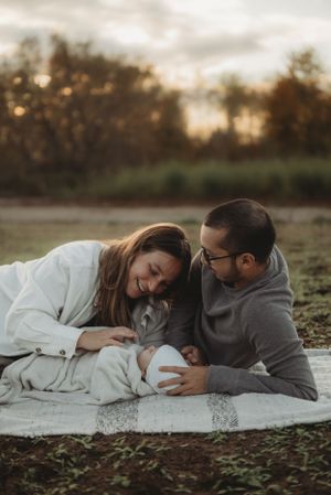Candid family moment with newborn baby on blanket in autumn field.