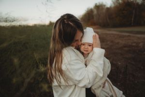 Parent holding and embracing baby wrapped in white on outdoor path at dusk.