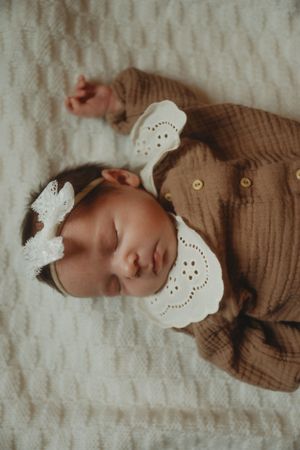 Sleeping newborn in brown outfit with white lace collar on textured blanket.