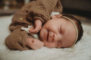 Sleeping baby wearing brown outfit nestled on white blanket.