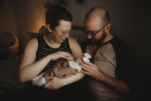 New parents tenderly feeding their newborn baby in a cozy, dimly lit room.
